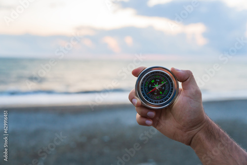 Holds a compass against the background of the sea