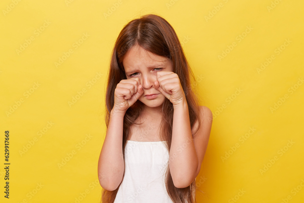 Unhappy sad little girl with long hair standing isolated over yellow background crying being offended expressing negative emotions. Unhappy sad little girl with long hair standing isolated over yellow background crying being offended expressing negative emotions.