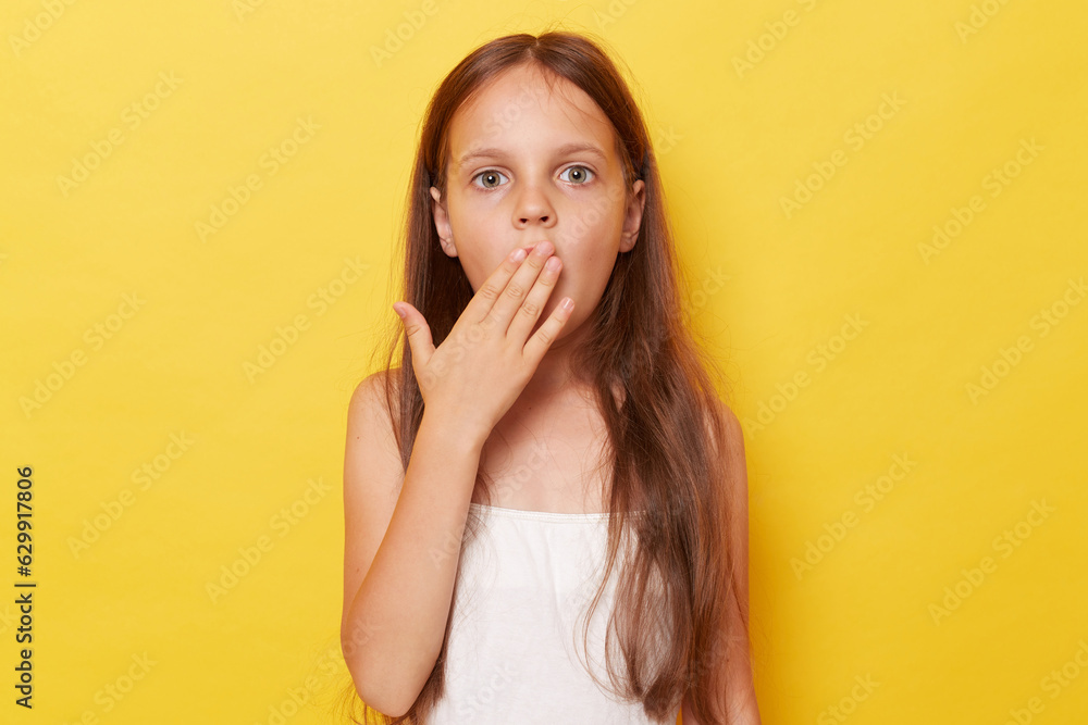 Surprised amazed little girl with long hair standing isolated over yellow background looking at camera with big eyes covering mouth sees something shocked. Surprised amazed little girl with long hair standing isolated over yellow background looking at camera with big eyes covering mouth sees something shocked.
