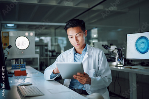 Tablet, planning and scientist with digital innovation, data and reading in laboratory. Asian man, doctor and information technology for futuristic medical research with pharma healthcare study photo