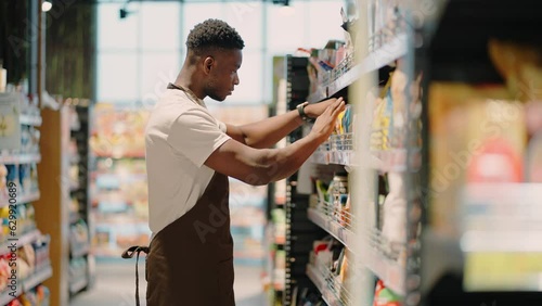 African American worker arranges goods on market shelf