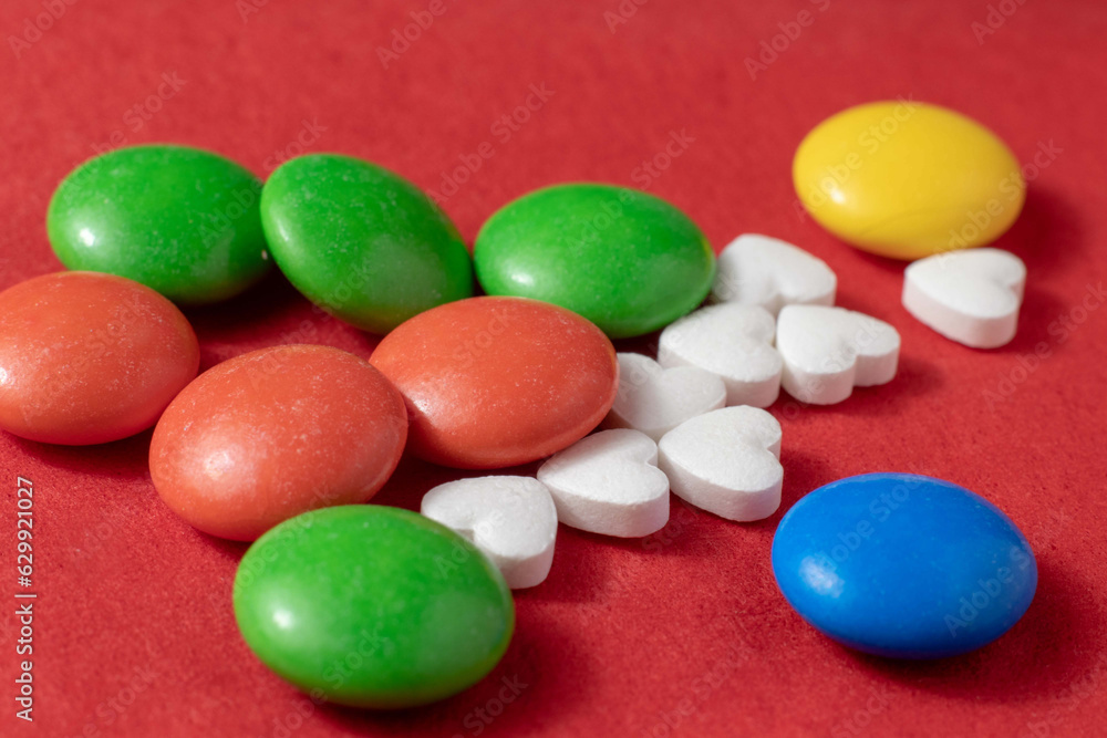 Close-up of a handful of heart-shaped pills and colored dragees on a red background. Close-up of a handful of heart-shaped pills and colored dragees on a red background.