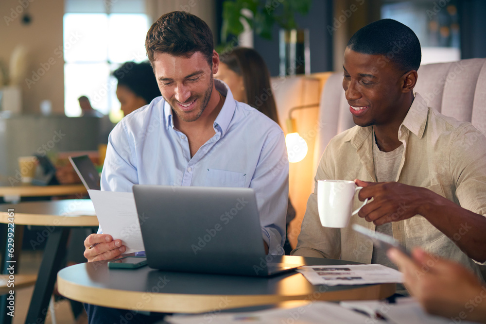 Fototapeta premium Two Businessmen Working On Laptop In Informal Seating Area Of Modern Office On Coffee Break