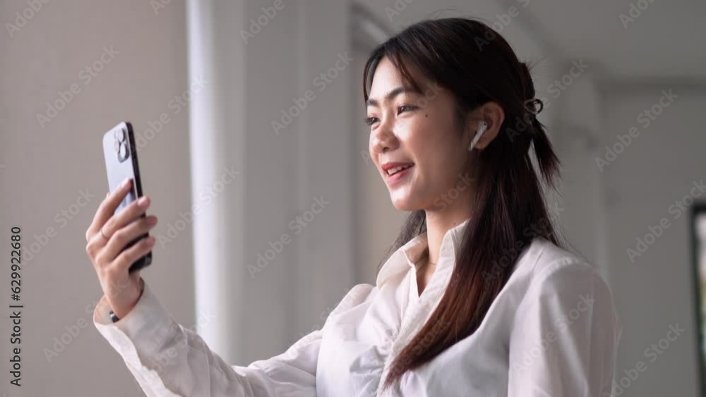 Video call, a young Asian woman communicates via smartphone wearing earbud having chat Video call, a young Asian woman communicates via smartphone wearing earbud having chat