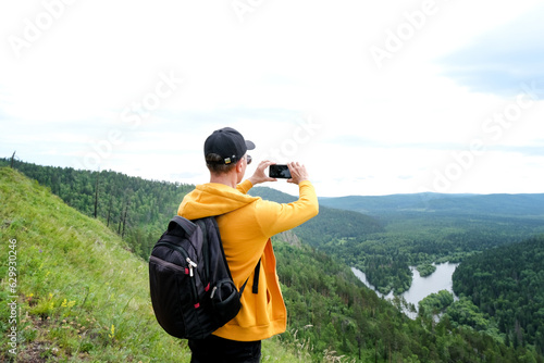 man with backpack taking selfie with mobile smart phone hiking mountains. Tourist looking at mountain beauty landscape from the top of hill.
