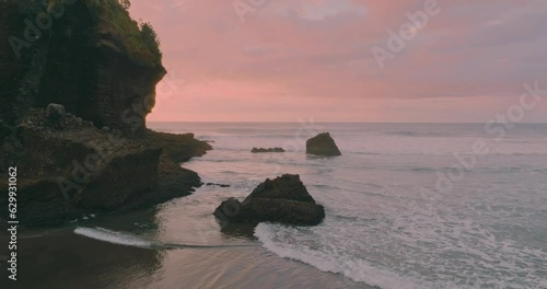 Aerial: Ocean waves crashing over rocks in slow motion at sunset