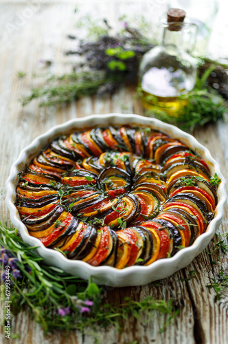 Traditional tian made of sliced vegetables in casserole dish on wooden table, focus on center part, close up view