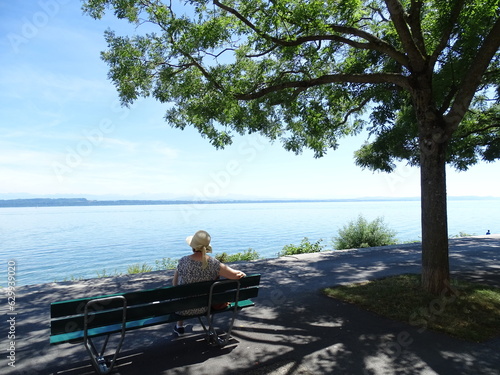 señora sentada y relajada en un banco delante de el lago con montañas de fondo, en suiza
