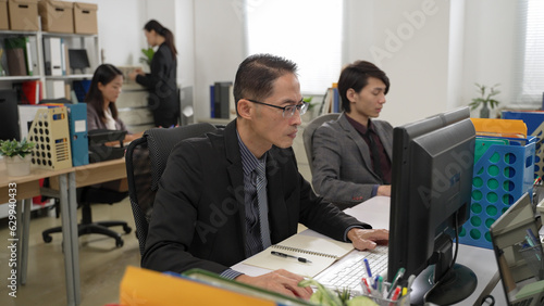 portrait of asian businessman wearing suit is writing notes and doing work on desktop computer with concentration in the office with other colleagues