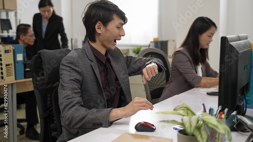 asian burnout male employee becoming energetic when he looks at watch and finds it’s time to get off duty. he leaves the office right away in a happy mood