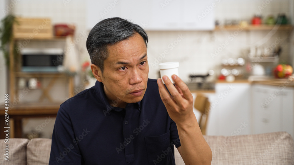 closeup of asian Japanese elderly male with presbyopia holding and looking at a pill container with confusion. He squints his eyes problem trying to see the instruction on bottle clearly closeup of asian Japanese elderly male with presbyopia holding and looking at a pill container with confusion. He squints his eyes problem trying to see the instruction on bottle clearly