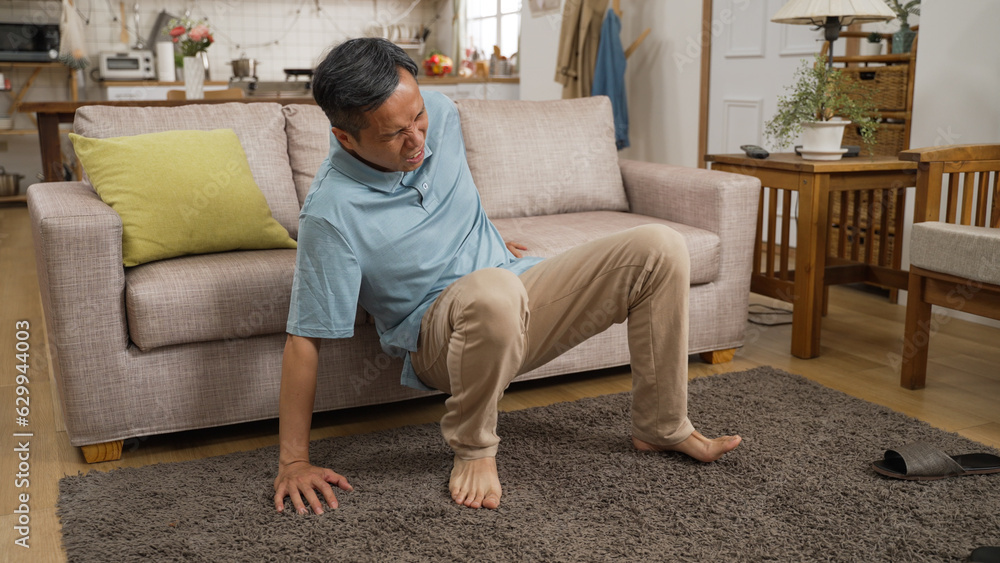 Asian painful senior man hurt his back after fall accident at home. he lets out a sigh after slowly moving to the sofa and sitting down for a rest.