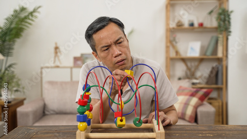 Closeup of Chinese retired Asian Parkinson’s patient undergoing rehab training with bead roller coater alone at home. his hand is shaking while practicing photo