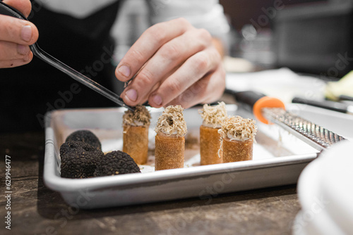 Photo of a chef's hands putting shredded truffle with tweezers on appetizers. photo