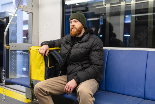 Wall Mural A bearded courier rides in a subway car next to a yellow thermos bag for transpo