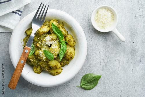 Potato gnocchi. Traditional homemade potato gnocchi with sauce pesto and basil in white plate on kitchen table on light grey kitchen table background. Traditional Italian food.  Top view.