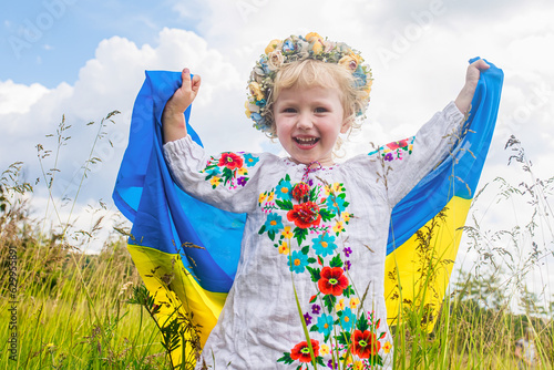 flag of Ukraine is on the shoulders of a little Ukrainian girl. Happy Ukrainian child in free Ukraine without war runs along a rural road photo