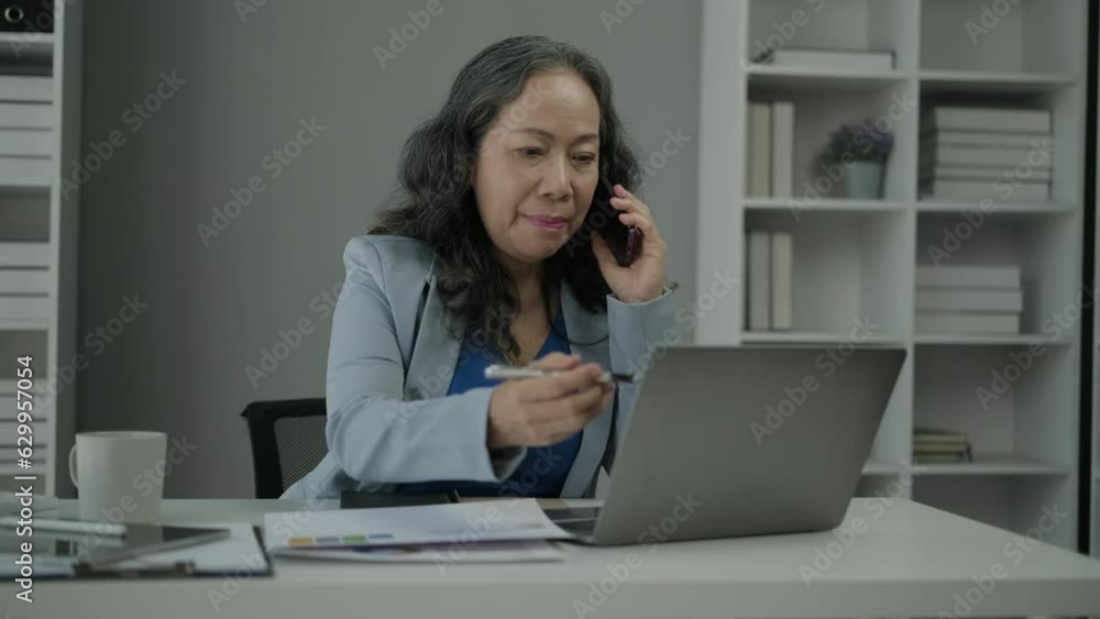 Middle age businesswoman having pleased phone conversation and checking online information on laptop Middle age businesswoman having pleased phone conversation and checking online information on laptop