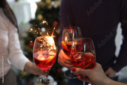Alcoholic cocktails and sparklers business team celebrates New Year. Three people hold glasses and clink glasses at Christmas or at party