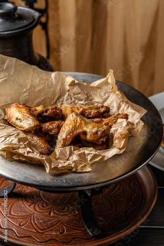 Turkish cuisine, fried chicken wings, lie on a special plate with coals on a dark background in a restaurant.