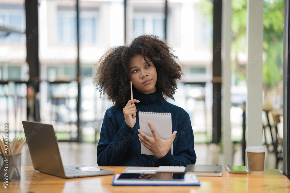 Portrait of a pretty young black woman a serious working on a laptop ...