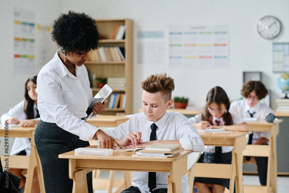 African American teacher talking to schoolboy during lesson at school