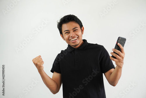 Excited happy young asian man winner feeling joy using smartphone winning lottery game, betting, getting cash back online gift in mobile app message holding cell phone isolated on white background.