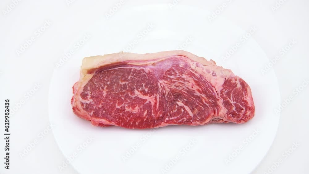 New york strip steak boneless meat cut macro closeup on plate with hand holding isolated on white background New york strip steak boneless meat cut macro closeup on plate with hand holding isolated on white background