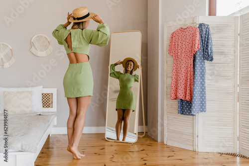 Foto young pretty woman in green dress trying on style trend dress looking in mirror
