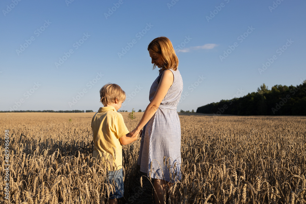 mother and son holding hands stand among spikelets in a wheat field. enjoy nature and life, togetherness. Earth Day. Stop the war in Ukraine. Back view. Stand with Ukraine