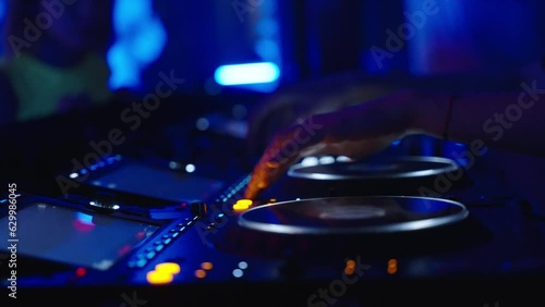 In the dark, a DJ console in a nightclub. Female DJ hands control the DJ console while dancing in a disco