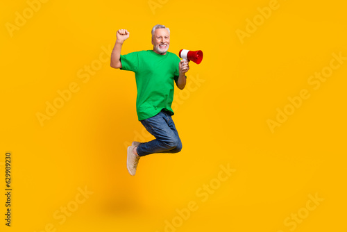 Full size profile photo of overjoyed energetic grandfather jumping hold loudspeaker toa empty space isolated on yellow color background