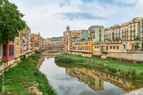 Colorful yellow and orange houses and bridge Pont de Sant Agusti reflected in water river Onyar, in Girona, Catalonia, Spain. Church of Sant Feliu and Saint Mary Cathedral at background. BRIDGE in the photo