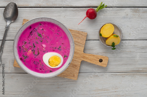 Chłodnik, Šaltibarščiai is traditional lithuanian, polish beet soup. Cold summer soup of beetroot, kefir, cucumbers, eggs, dill and potatoes in a bowl on a cutting board. Summer Healthy food. Top view photo