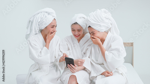 Group of women in bathrobes merrily watching social media together on mobile phone.