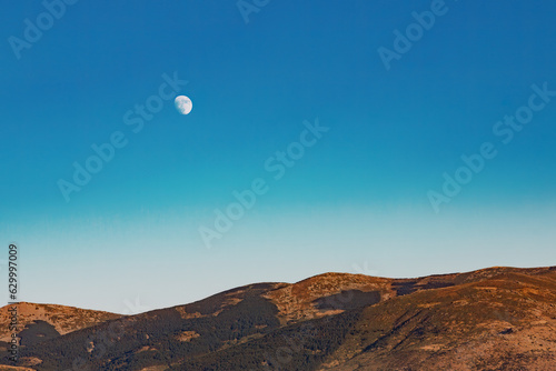 Moonrise over the mountains against the blue sky.