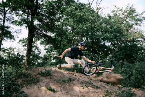 Young man in helmet riding bmx bike in forest, doing dangerous tricks and falling down. Difficult training before race. Concept of active lifestyle, sport, extreme, dynamics, hobby, freestyle