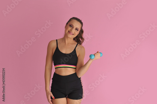 mulher com roupa de treino fitness segurando peso de academia em fundo rosa  photo