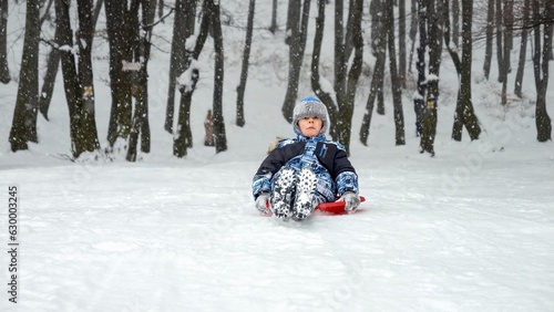 Boy gleefully gliding down a snow-covered hill on his plastic sled, grinning from ear to ear. The perfect image of winter holidays, fun in the snow, and the joy of childhood.