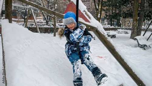 Cheerful smiling boy riding on the zipline at public playground on a snowy winter day photo