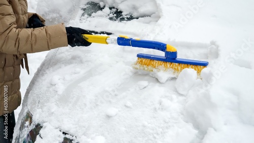 Close-up of a young woman cleaning off snow from her car with a brush. Concept of winter, vehicle maintenance, and daily chores.