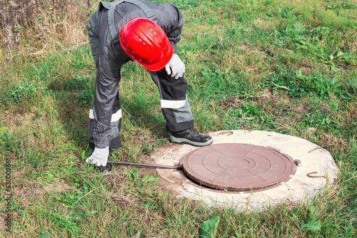 Fotografía A worker in overalls and a helmet opens a manhole with a crowbar