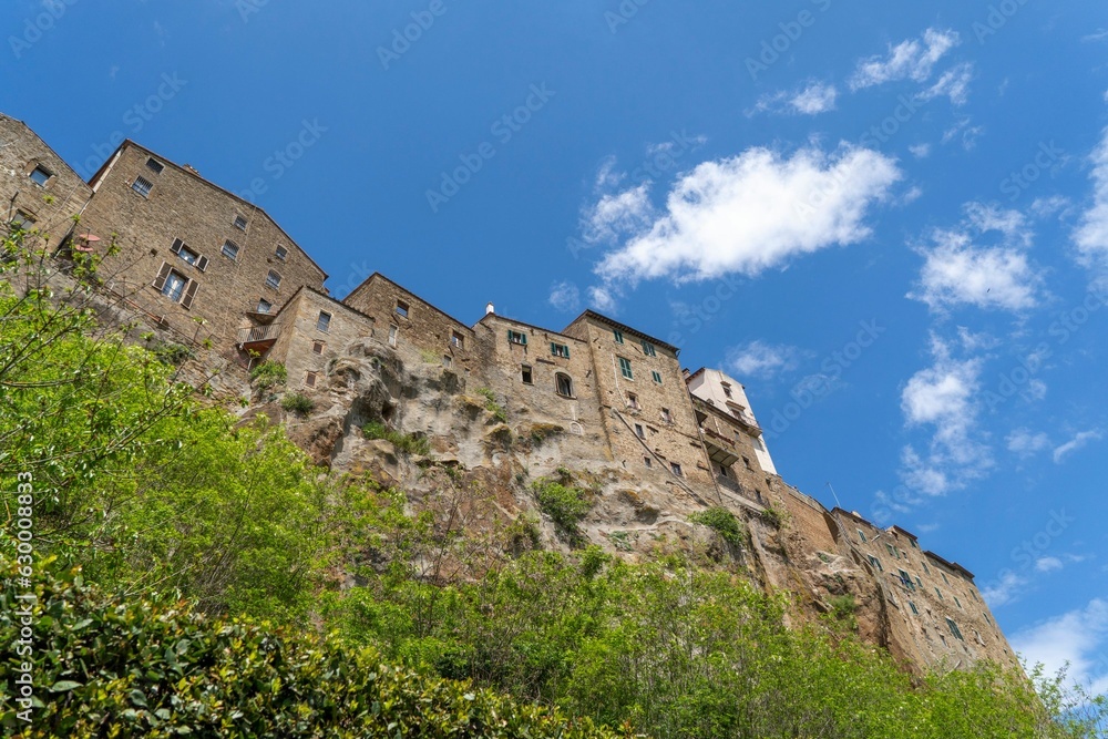 Low-angle view of the buildings of Pitigliano standing on a lush hill