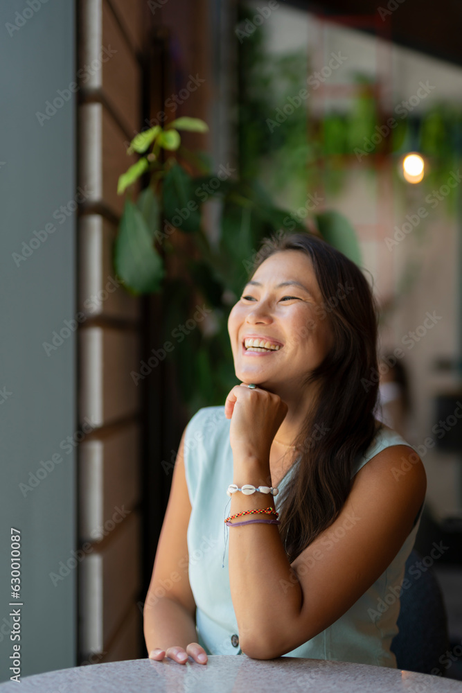 A young cheerful Asian woman sits at a table in a cafe. A young cheerful Asian woman sits at a table in a cafe.