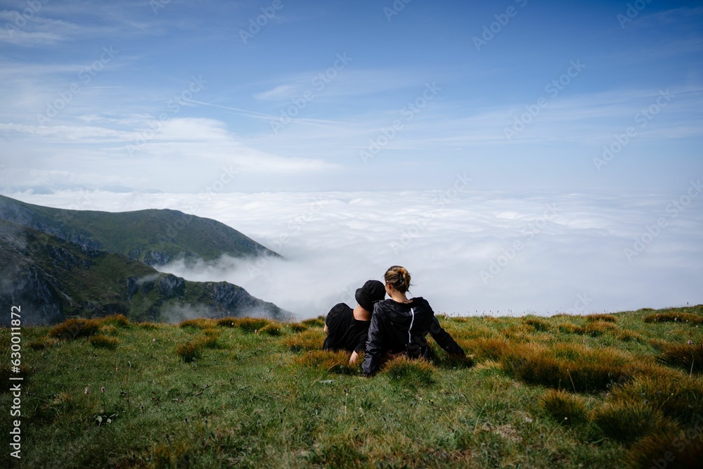 Couple sitting on the mountain field above the clouds.