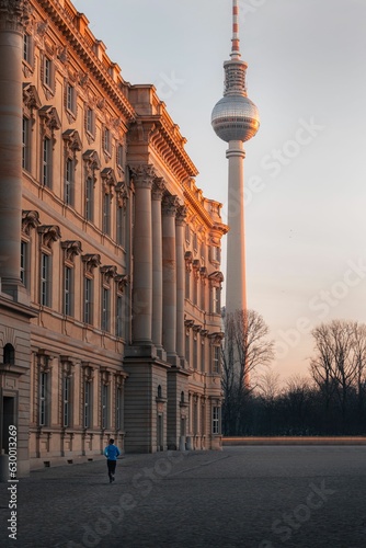 Photography man in blue running on pavement in front of large beige building with tv tower