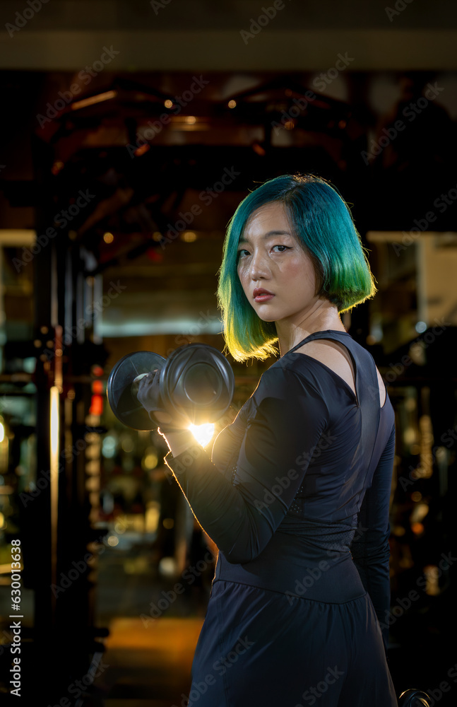 Fototapeta premium fashion hairstyle asian woman lifting dumbbell in one hand energizing strong exercise at modern gym, active fitness people workout functional training for body and mental health in dark sport club