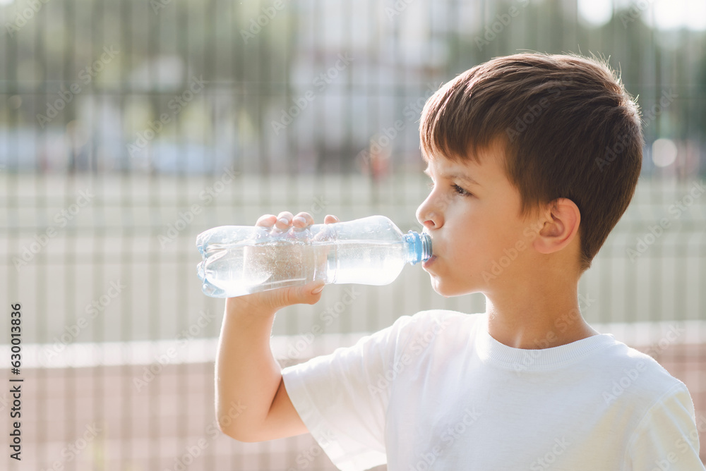 Cute child drinks water from a bottle on the street in summer Cute child drinks water from a bottle on the street in summer