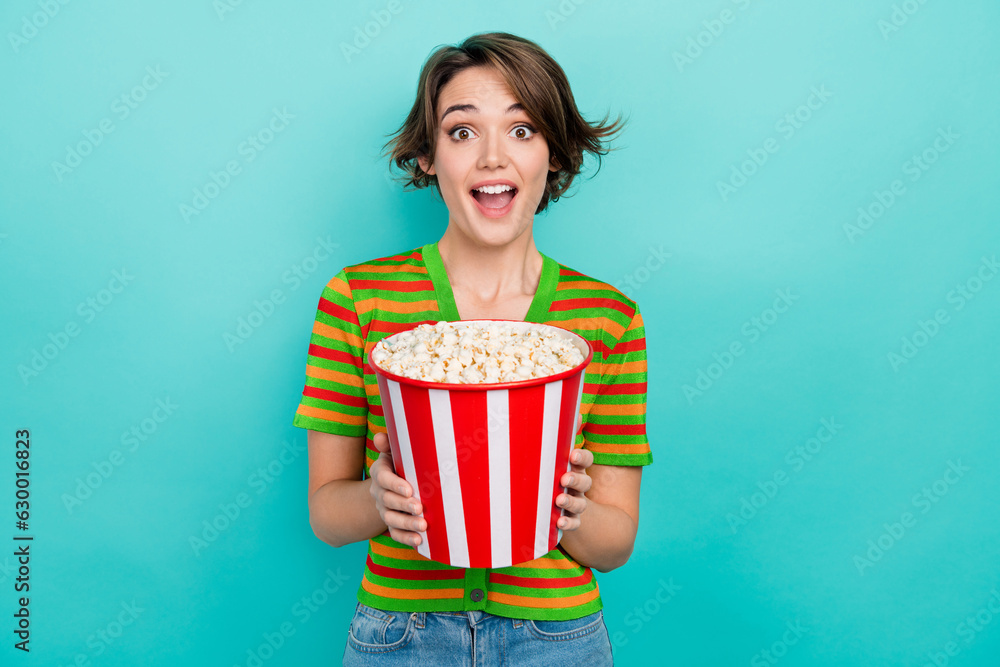 Portrait of astonished cheerful girl hands hold big popcorn bucket isolated on turquoise color background