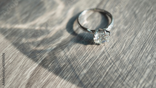 Close up of diamond ring on wood desk with sunlight and shadow. Love, valentine, relationship and wedding concept. Soft and selective focus.